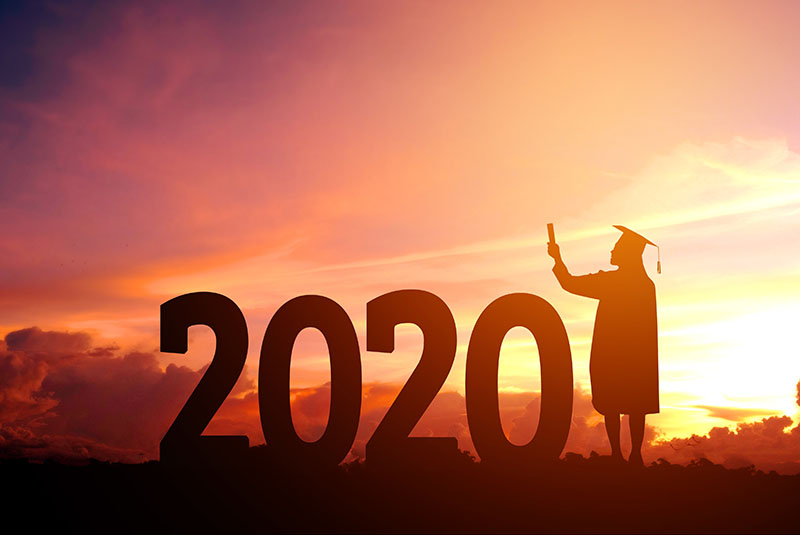 A graduate looking off into the sunset next to a 2020 sign.